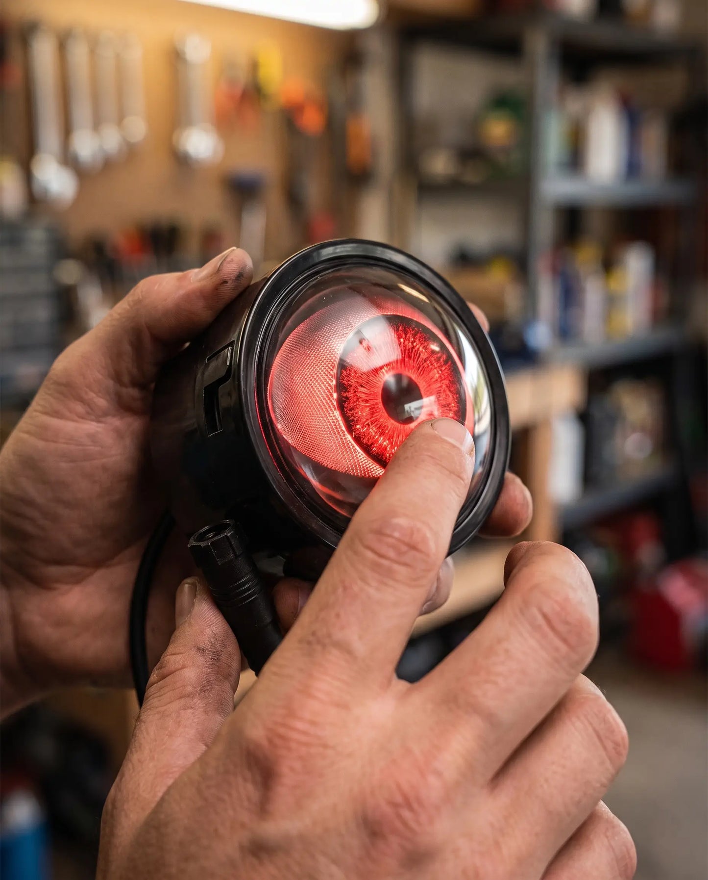 Close-up of hands holding Nyxora Demon-Eye LED headlight unit with glowing red iris lens