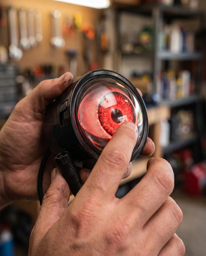 Close-up of hands holding Nyxora Demon-Eye LED headlight unit with glowing red iris lens